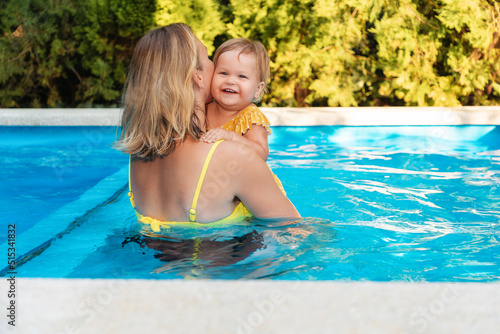 Children's day. A woman hugs a happy little child while swimming in the pool. View from the back. The concept of a joyful childhood