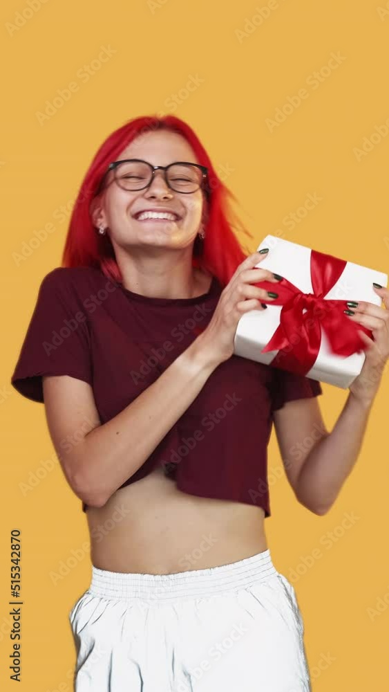 Vertical video. Holiday present. Festive fun. Anniversary party. Overjoyed grateful happy birthday girl jumping with wrapped gift box on orange background. Vertical video. Holiday present. Festive fun. Anniversary party. Overjoyed grateful happy birthday girl jumping with wrapped gift box on orange background.