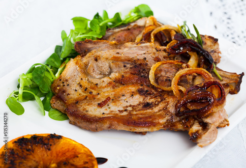Image of tasty cooked fried pork chop with fried orange, onion and greens at plate