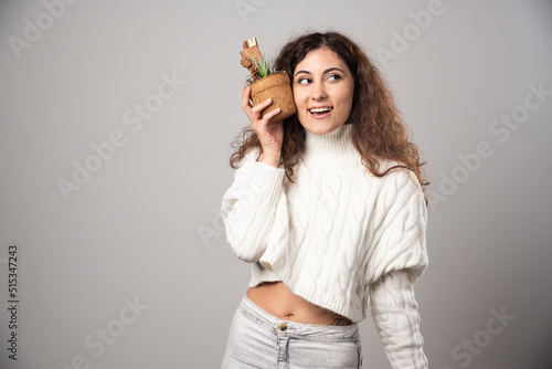 Young woman gardener holding a plant on a gray wall