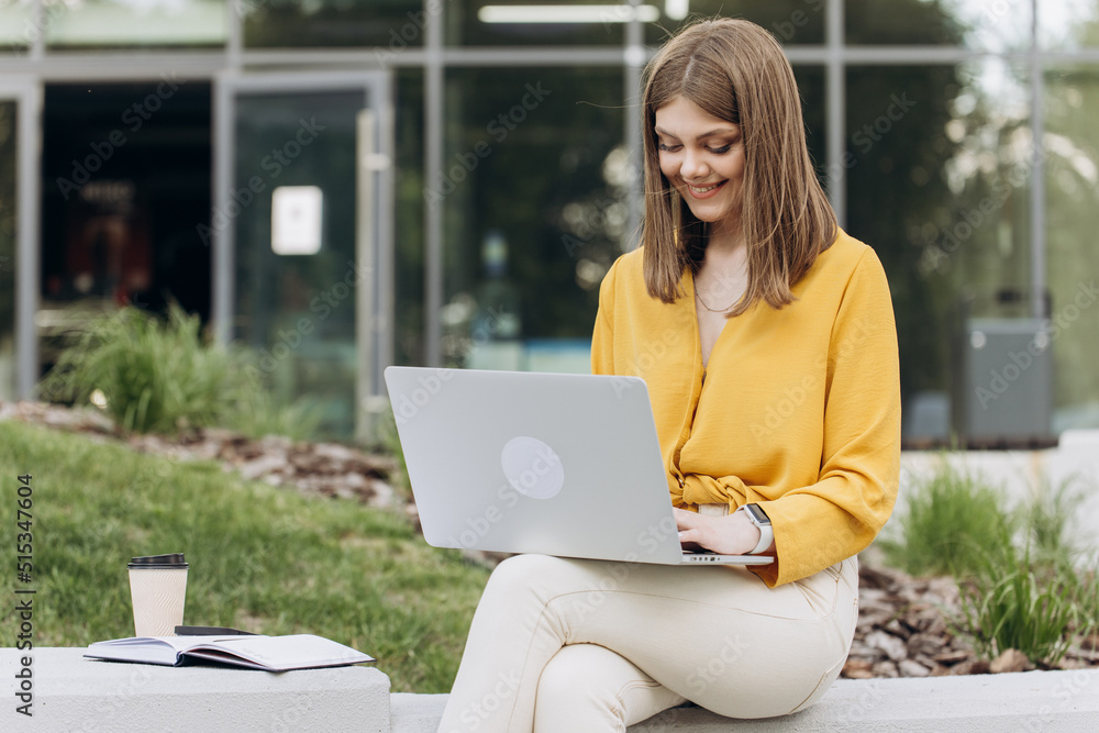 Attractive young female using laptop while sitting on bench outdoors in city. Pretty girl student preparing for classes in nature. Lady corporate start up office employee working outdoor. Attractive young female using laptop while sitting on bench outdoors in city. Pretty girl student preparing for classes in nature. Lady corporate start up office employee working outdoor.