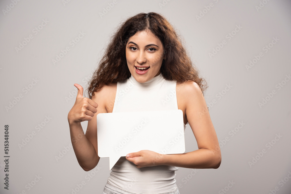 Young woman showing a thumb up and holding blank white poster Young woman showing a thumb up and holding blank white poster