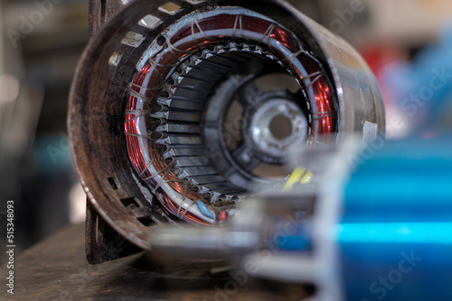 Old and rusted electric motor windings placed on a workbench with blurred stator. Industrial Generator Maintenance Concept photo