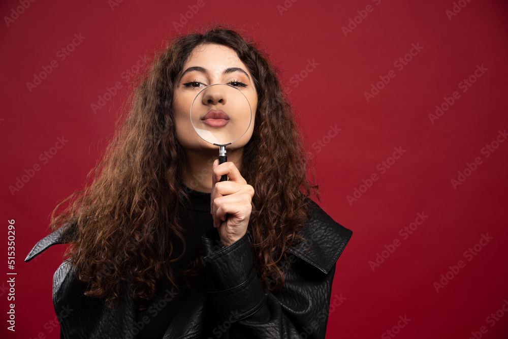 Woman holding a magnifying glass on the red background Woman holding a magnifying glass on the red background