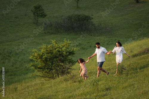 cheerful family holding hands while running on grassy slope on summer day.