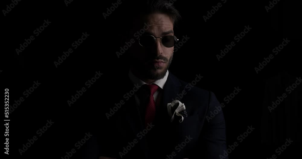 mysterious businessman pulling down sunglasses and looking over, looking to side and arranging tie while posing on black background mysterious businessman pulling down sunglasses and looking over, looking to side and arranging tie while posing on black background