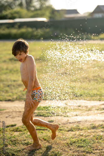 boys are doused with cold water from a hose. Summer fun in the village, happy kids fooling around and laughing. Teenager runs emotionally under splashes of cold water
