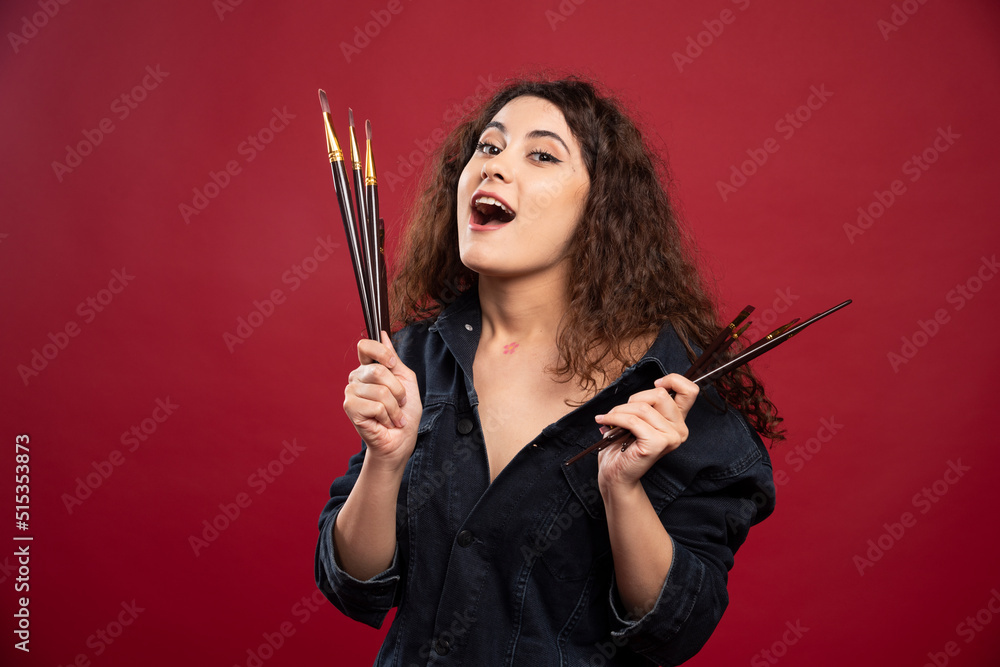 Female artist holding paintbrushes on red background Female artist holding paintbrushes on red background