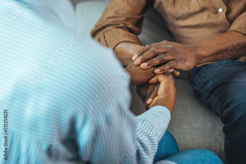 Close up black woman and man sitting on couch two people holding hands. Symbol sign sincere feelings, compassion, loved one, say sorry. Reliable person, trusted friend, true friendship concept