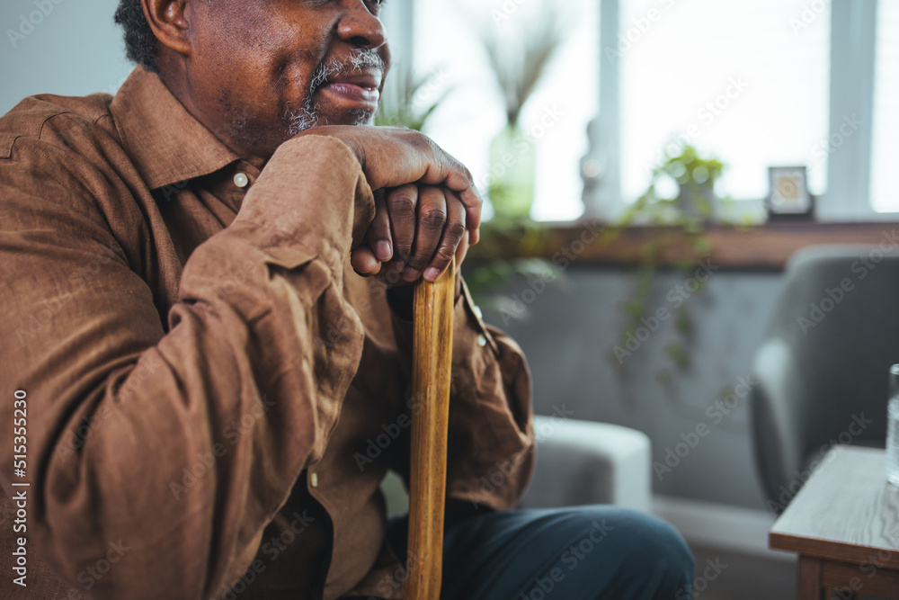 Thoughtful elderly man sitting alone at home with his walking cane ...