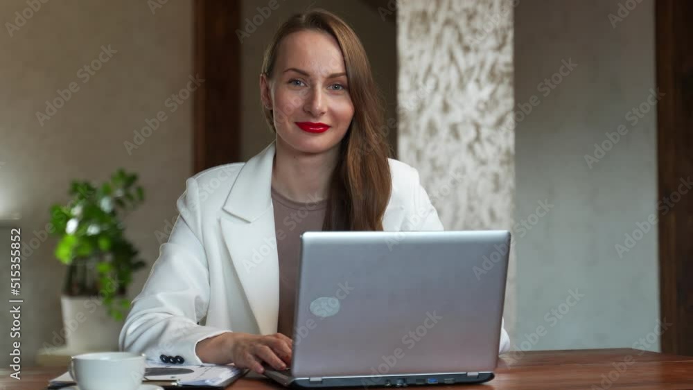 A successful young woman working at her office desk. A woman is sitting at a table and looking at the camera. A successful young woman working at her office desk. A woman is sitting at a table and looking at the camera.