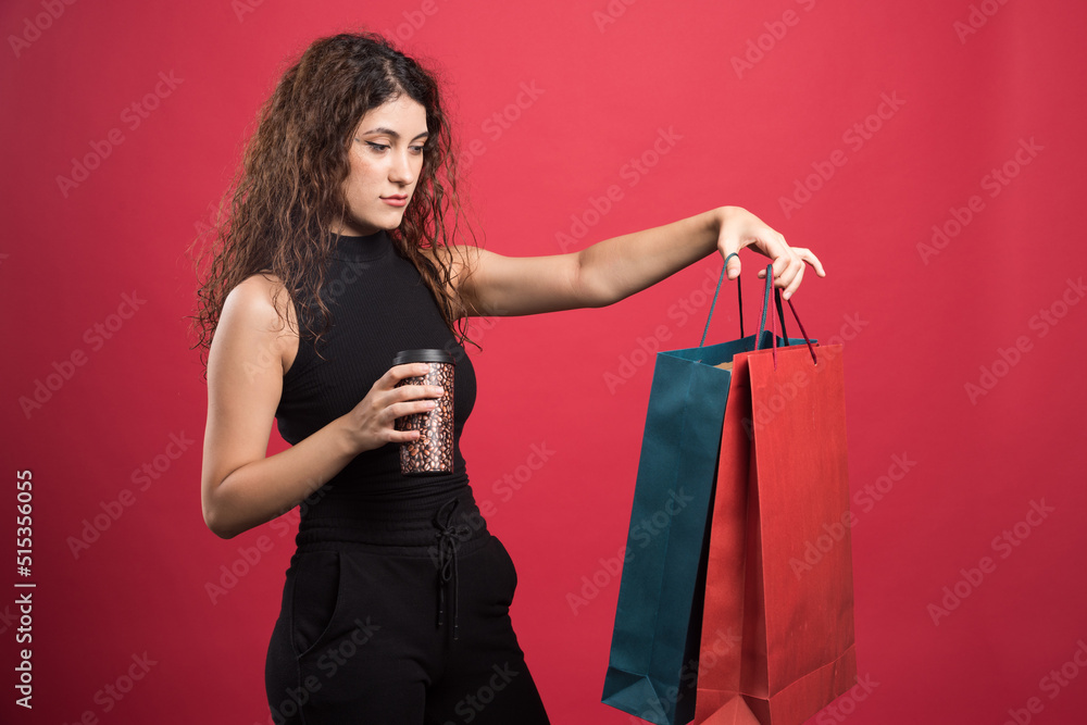 Naklejka premium Woman with cup showing her two bags of new clothes on red background