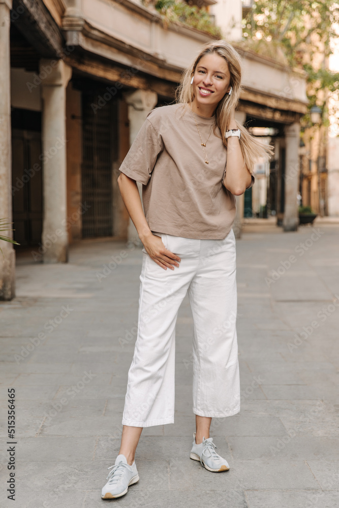 Full-lengths view of smiling beautiful woman staying at the street . Caucasian fair-skinned lady wearing casual clothes in headphones Full-lengths view of smiling beautiful woman staying at the street . Caucasian fair-skinned lady wearing casual clothes in headphones