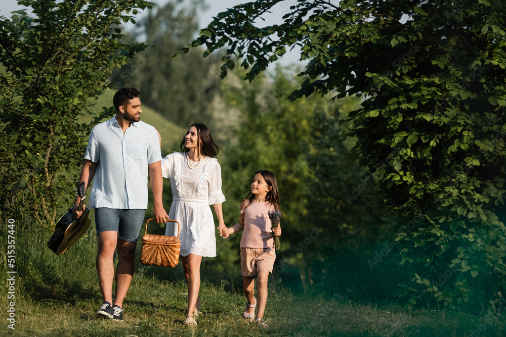 full length of happy man with acoustic guitar and wicker basket walking with family outdoors. full length of happy man with acoustic guitar and wicker basket walking with family outdoors.