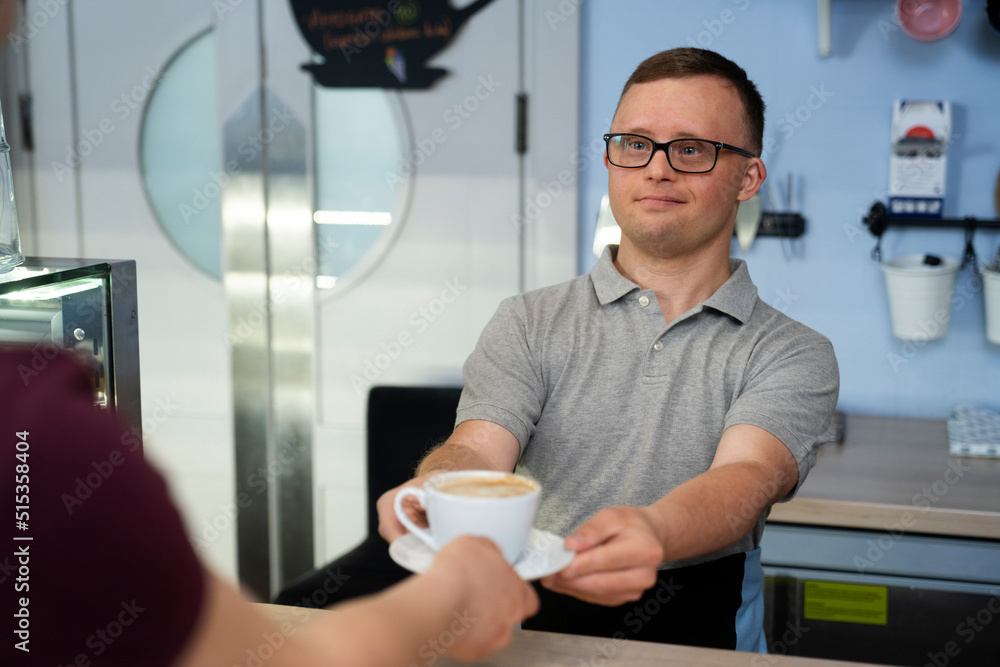 Caucasian man with down syndrome serving a cup of coffee to the client Caucasian man with down syndrome serving a cup of coffee to the client