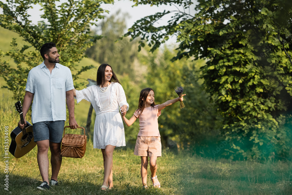 Fototapeta premium girl pointing with finger near parents walking with wicker basket and acoustic guitar.
