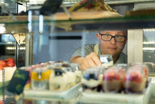 Caucasian man with down syndrome picking a dessert from the fridge to serve in a cafe