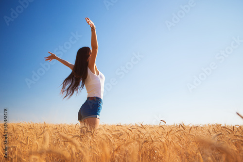 Happy woman enjoying the life in the field. Nature beauty, blue sky, white clouds and field with golden wheat. Outdoor lifestyle. Freedom concept. Woman jump in summer field © Dmytro Sunagatov