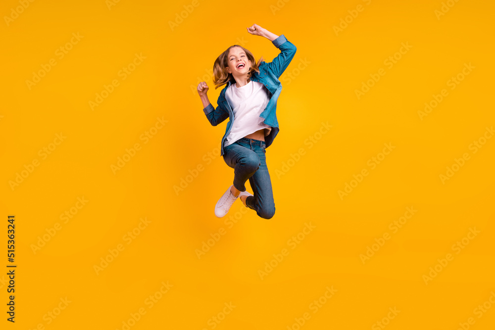 Obraz premium Full length portrait of overjoyed delighted girl raise fists celebrate achievement jumping isolated on yellow color background