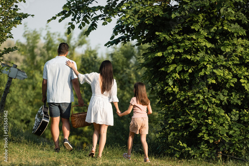 back view of man with wicker basket and acoustic guitar walking with family outdoors. © LIGHTFIELD STUDIOS