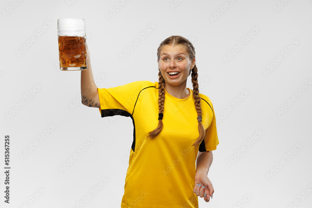 One young excited woman in yellow football kit holding beer mug and supports favorite team. Soccer fans, competition, sport, oktoberfest concept One young excited woman in yellow football kit holding beer mug and supports favorite team. Soccer fans, competition, sport, oktoberfest concept