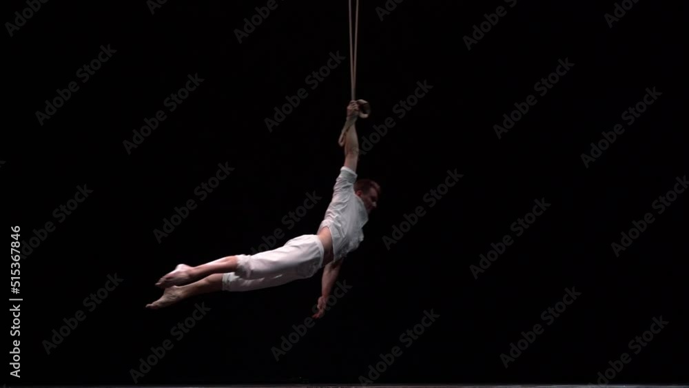 Muscular circus artist perform on the aerial straps on black background. Movement, strength concept Muscular circus artist perform on the aerial straps on black background. Movement, strength concept