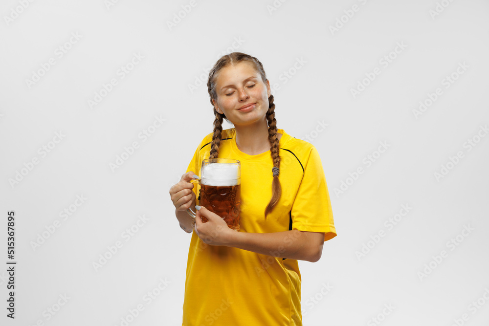 One young excited woman in yellow football kit holding beer mug and supports favorite team. Soccer fans, competition, sport, oktoberfest concept One young excited woman in yellow football kit holding beer mug and supports favorite team. Soccer fans, competition, sport, oktoberfest concept