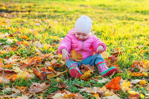 Happy young girl playing under falling yellow leaves in beautiful autumn park on nature walks outdoors. Little child throws up autumn orange maple leaves. Hello autumn concept