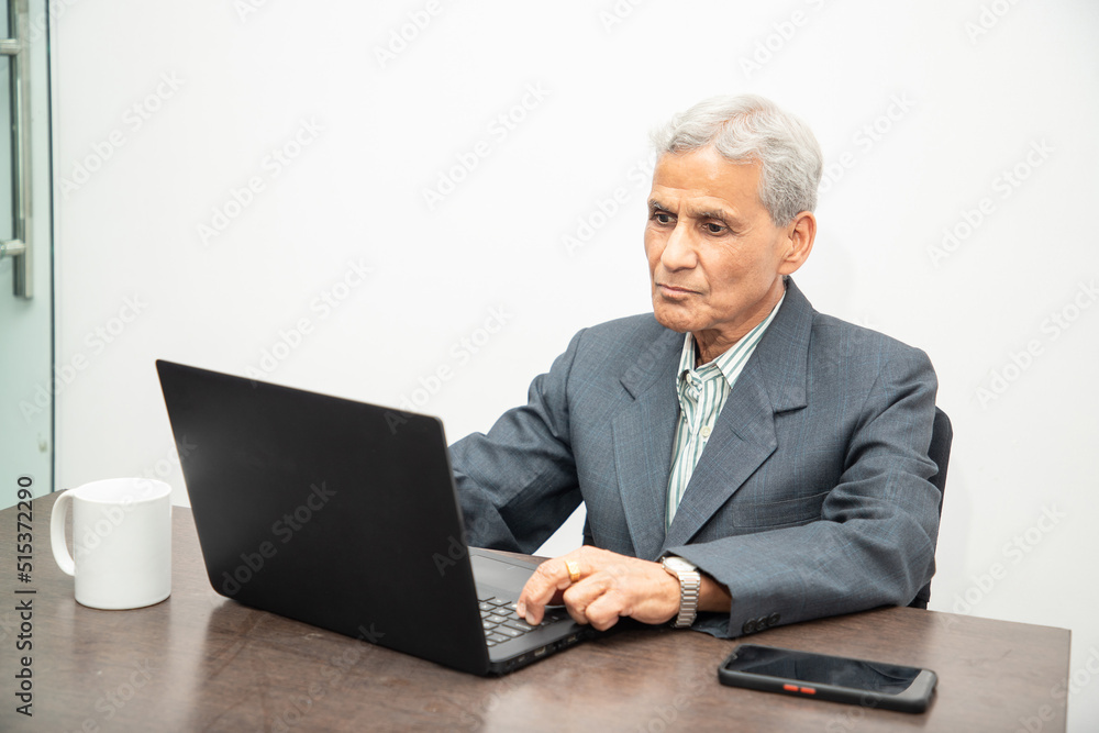 Senior Indian businessman working on a laptop in office. Elderly mature gray haired asian corporate male using computer. Senior Indian businessman working on a laptop in office. Elderly mature gray haired asian corporate male using computer.