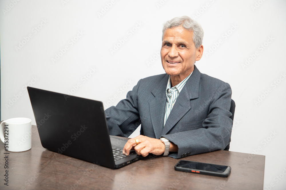 Portrait of happy senior Indian businessman working on a laptop in office. Elderly mature gray haired asian corporate male using computer. Portrait of happy senior Indian businessman working on a laptop in office. Elderly mature gray haired asian corporate male using computer.