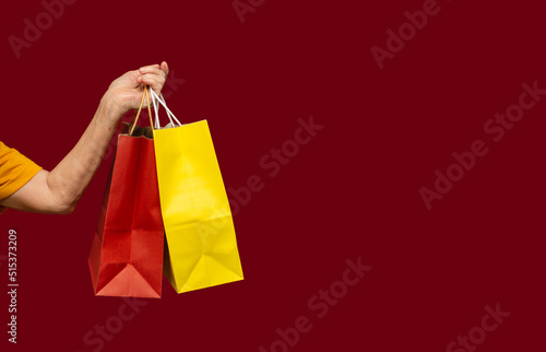 Close-up of hand holding yellow and red shopping bags with a handle while standing on a red background