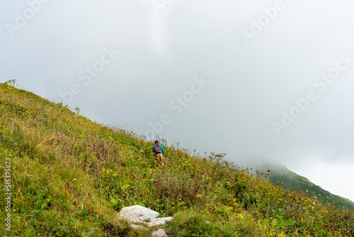 Rear view young man with a backpack walking uphill on a mountain path in fog among lush vegetation healthy and active lifestyle hiking outdoor activities, landscape