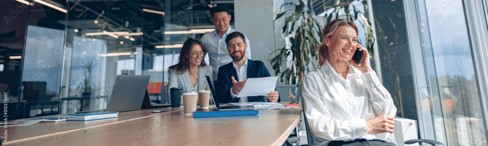 Smiling businesswoman is sitting on a chair and talking on phone during meeting in modern office Smiling businesswoman is sitting on a chair and talking on phone during meeting in modern office
