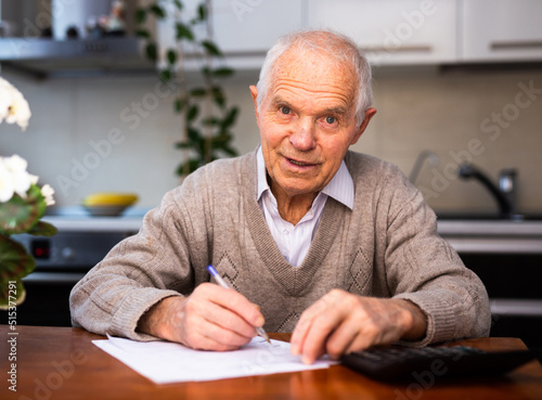 elderly pensioner writing on piece of paper at table in kitchen