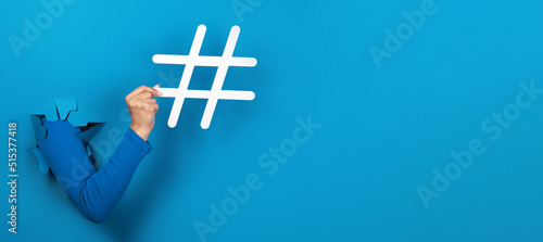 hand holding hashtag sign over blue background, social media concept, panoramic layout