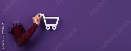 Foto hand holding shopping cart over purple background, panoramic layout