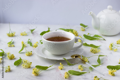 Tea with linden in a white cup on a white marble table. White teapot with aromatic tea