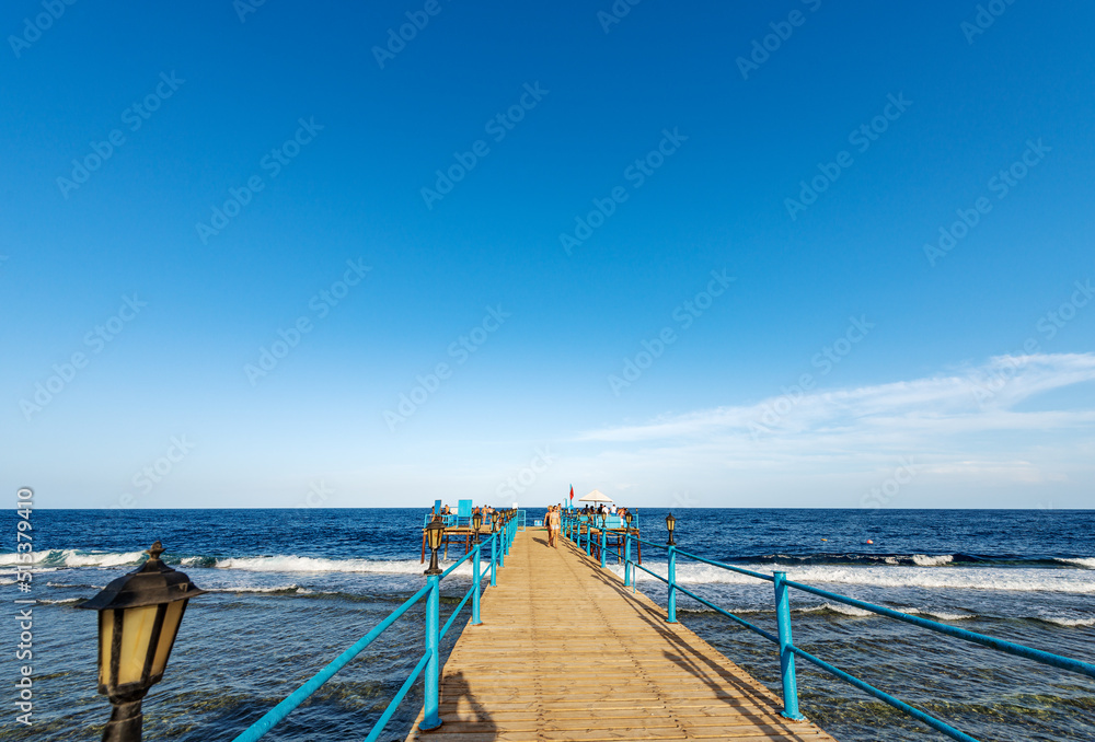 Seascape of the Red Sea near Marsa Alam, Egypt, Africa. Wooden pier above the coral reef used for diving, snorkeling and swimming with a group of tourists.