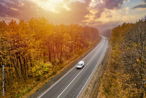 Wallpaper Mural white car driving on the asphalt road through the autumn forest at sunset