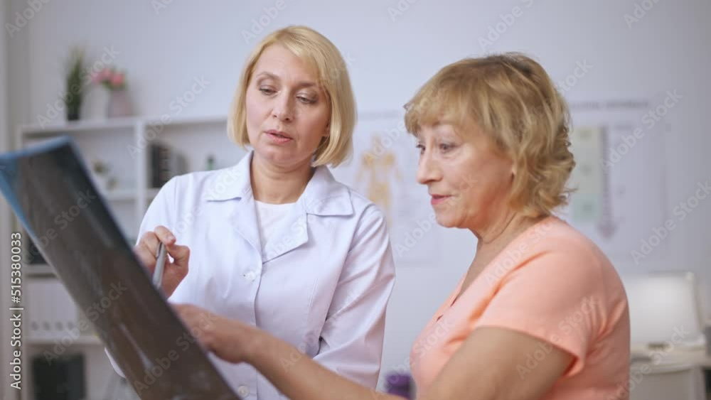 Happy senior patient and nice female doctor discussing x-ray image and smiling Happy senior patient and nice female doctor discussing x-ray image and smiling