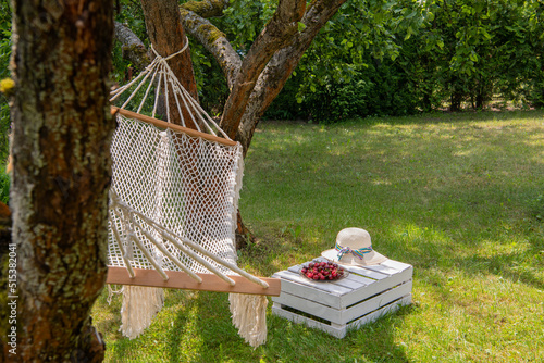 Relaxing in the garden - a hammock, cherries on a wooden plate on a plate and a summer hat next to it