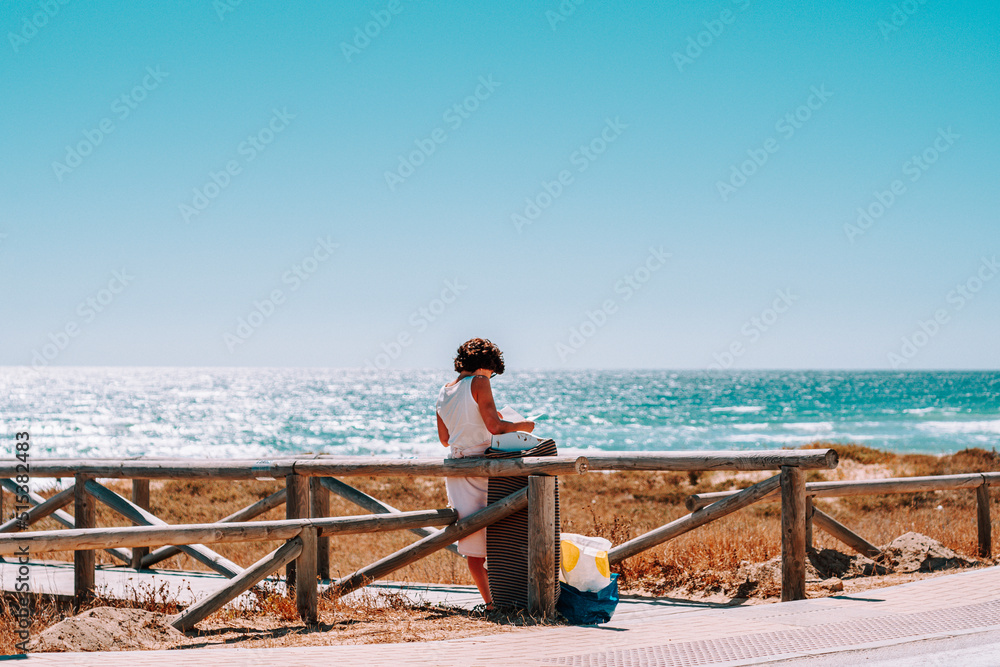 mujer de espaldas leyendo en el camino de madera en la playa