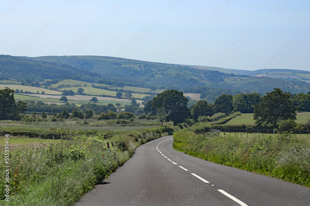 Downhill on an empty road in Somerset, England. Lush green rolling hills of the Quantocks can be seen in the background