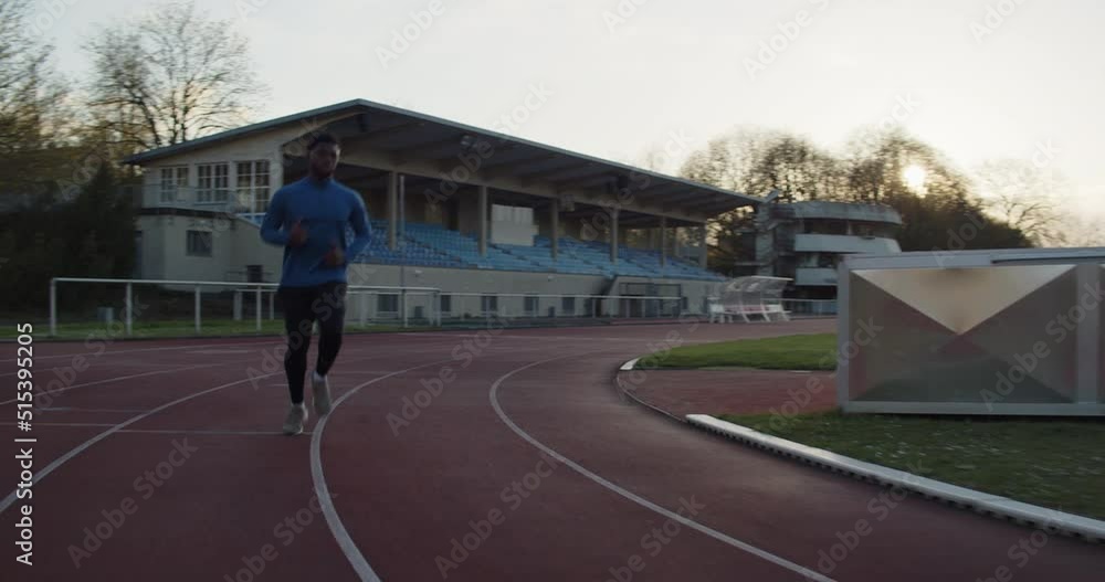 A cinematic shot of young black male running on empty running track with the sun setting in the background. A cinematic shot of young black male running on empty running track with the sun setting in the background.