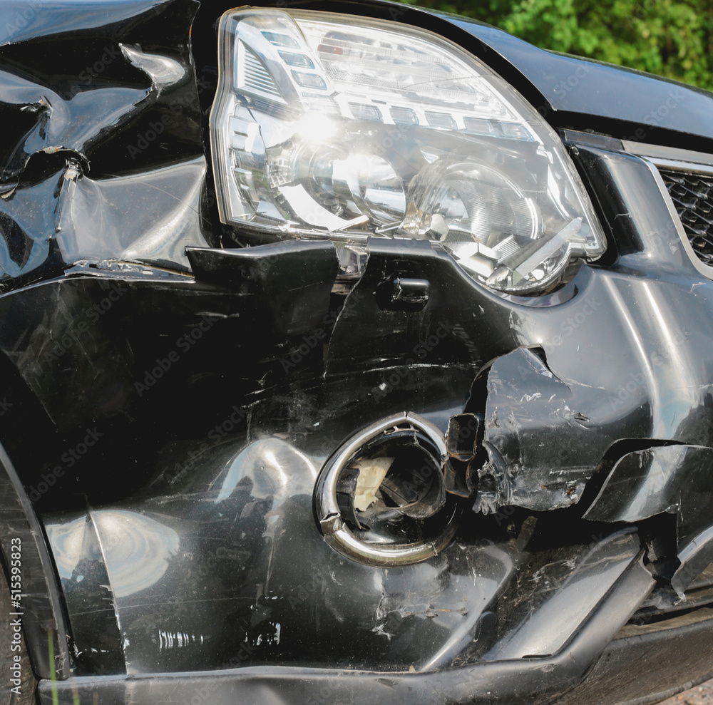 The front part of the black car is damaged as a result of a traffic accident. The front part of the car is black, damaged and broken as a result of the accident. Hood, headlight, bumper.
