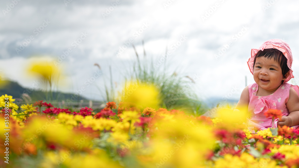 Fototapeta premium A baby girl in pink dress enjoy playing at colorful flower garden with cloudy sky as background. People in nature portrait photo. 