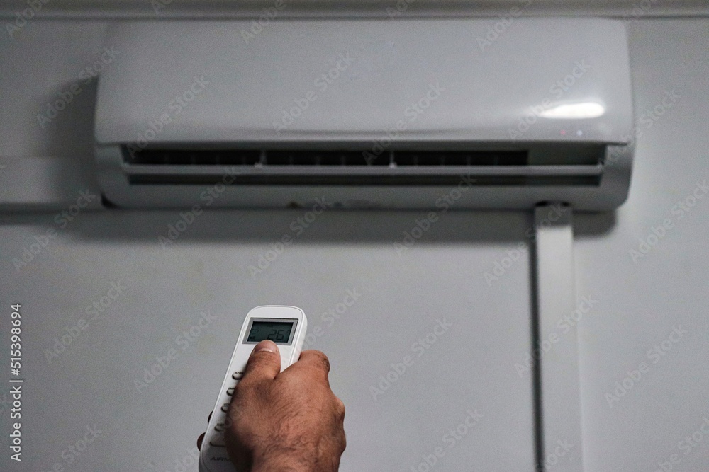 Fototapeta premium a hand of a man turning on the air-conditioning with the temperature of 26 degrees