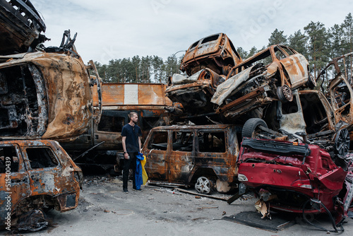 Man with Ukrainian flag stands against cars cemetery in Irpin. Consequences of the Russian military invasion in Ukraine.