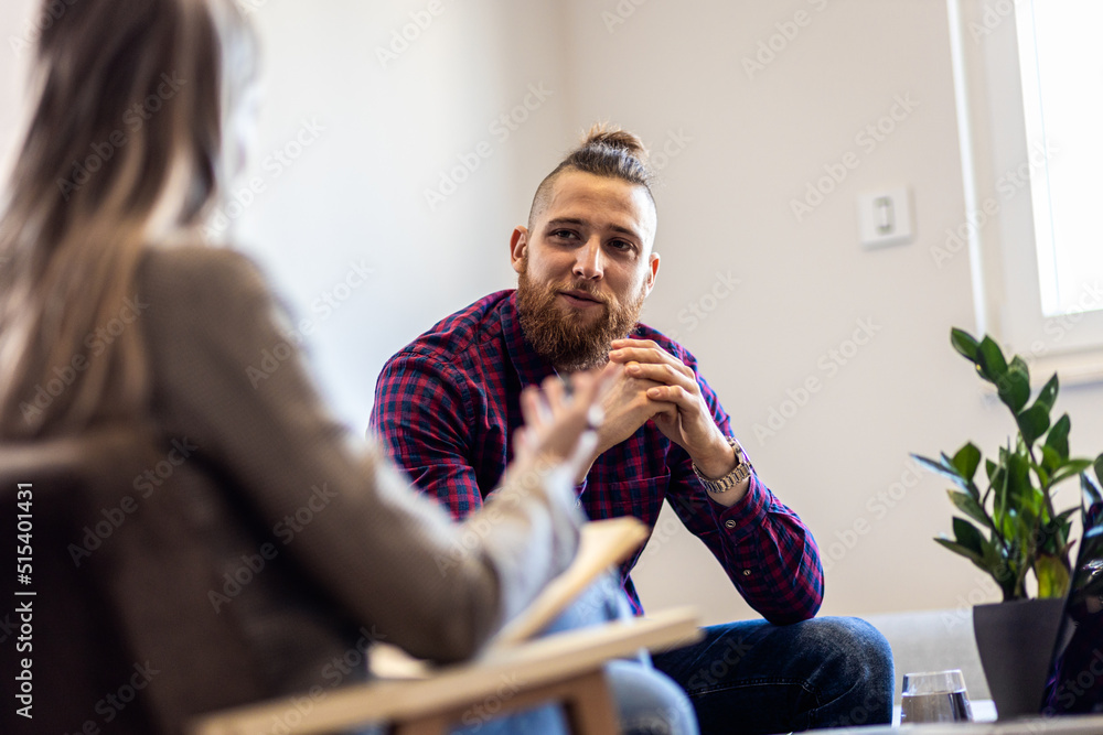 Young man talking to female psychologist during session. - obrazy, fototapety, plakaty 