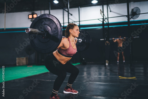 Powerful determined woman in sportswear weightlifting barbell equipment during gym workout in sportive studio interior, Caucasian female bodybuilder feeling energy and motivation during crossfit